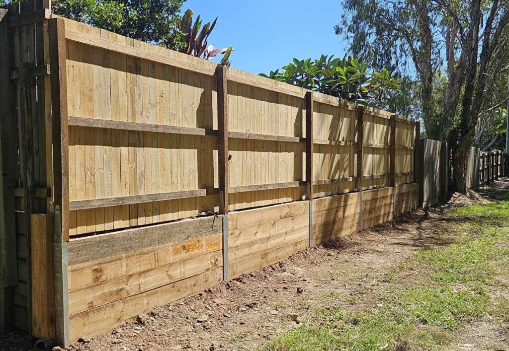 wooden fence made using pine palings and hardwood posts and rails. Fence is sitting on a pine sleeper retaining wall